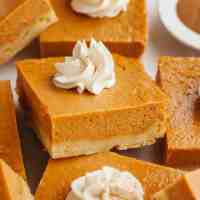 Several pumpkin pie bars topped with whipped cream.