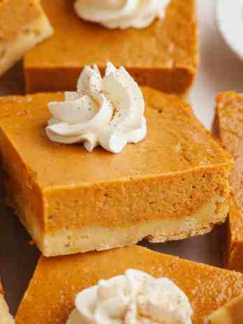 Several pumpkin pie bars topped with whipped cream.