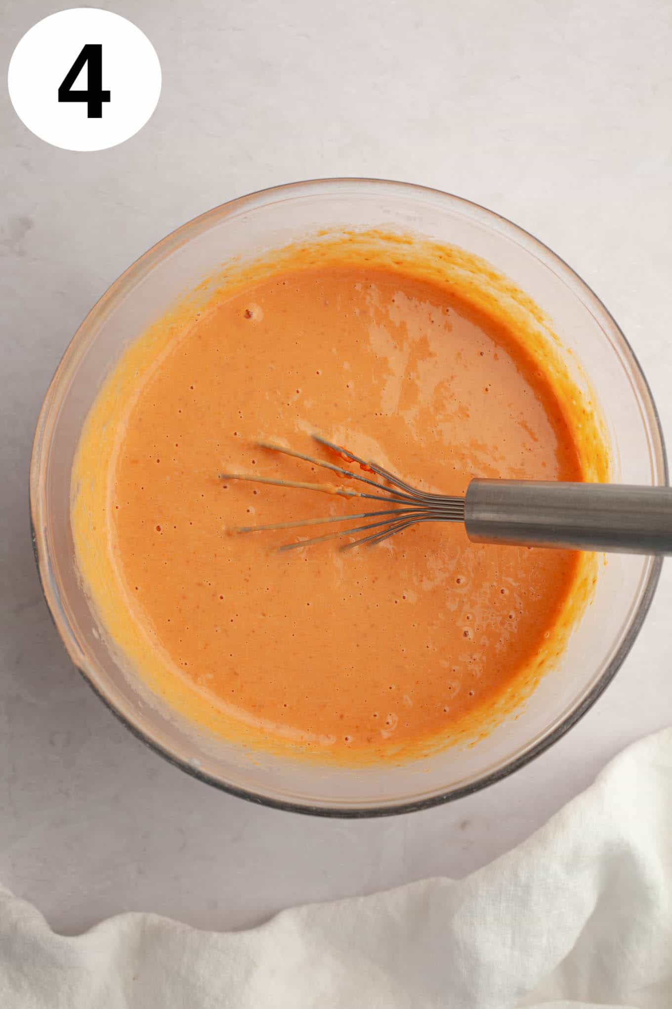 An overhead view of a pumpkin puree and egg mixture in a mixing bowl, with a whisk. 