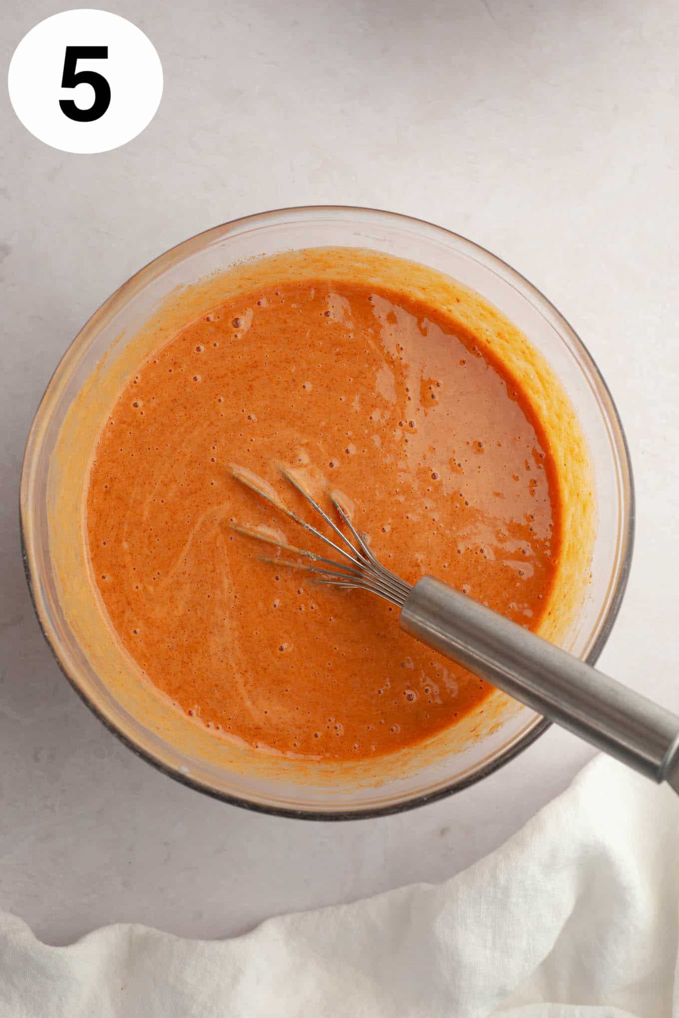 An overhead view of pumpkin pie filling in a mixing bowl, with a whisk. 