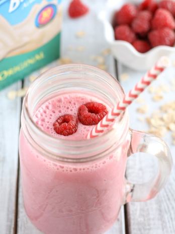 Overhead view of a raspberry almond milk smoothie next to a carton of almond milk and a bowl of fresh berries.