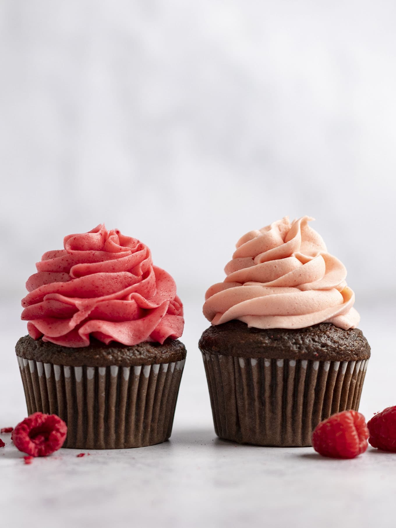 Two chocolate cupcakes topped with raspberry frosting, sitting side by side. 