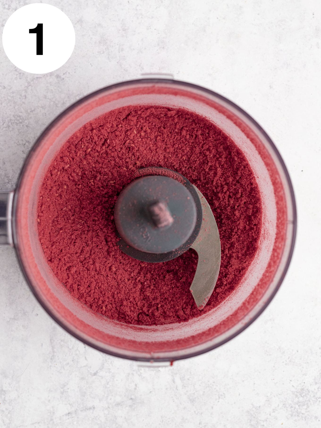 An overhead view of freeze-dried raspberry powder in the bowl of a food processor. 