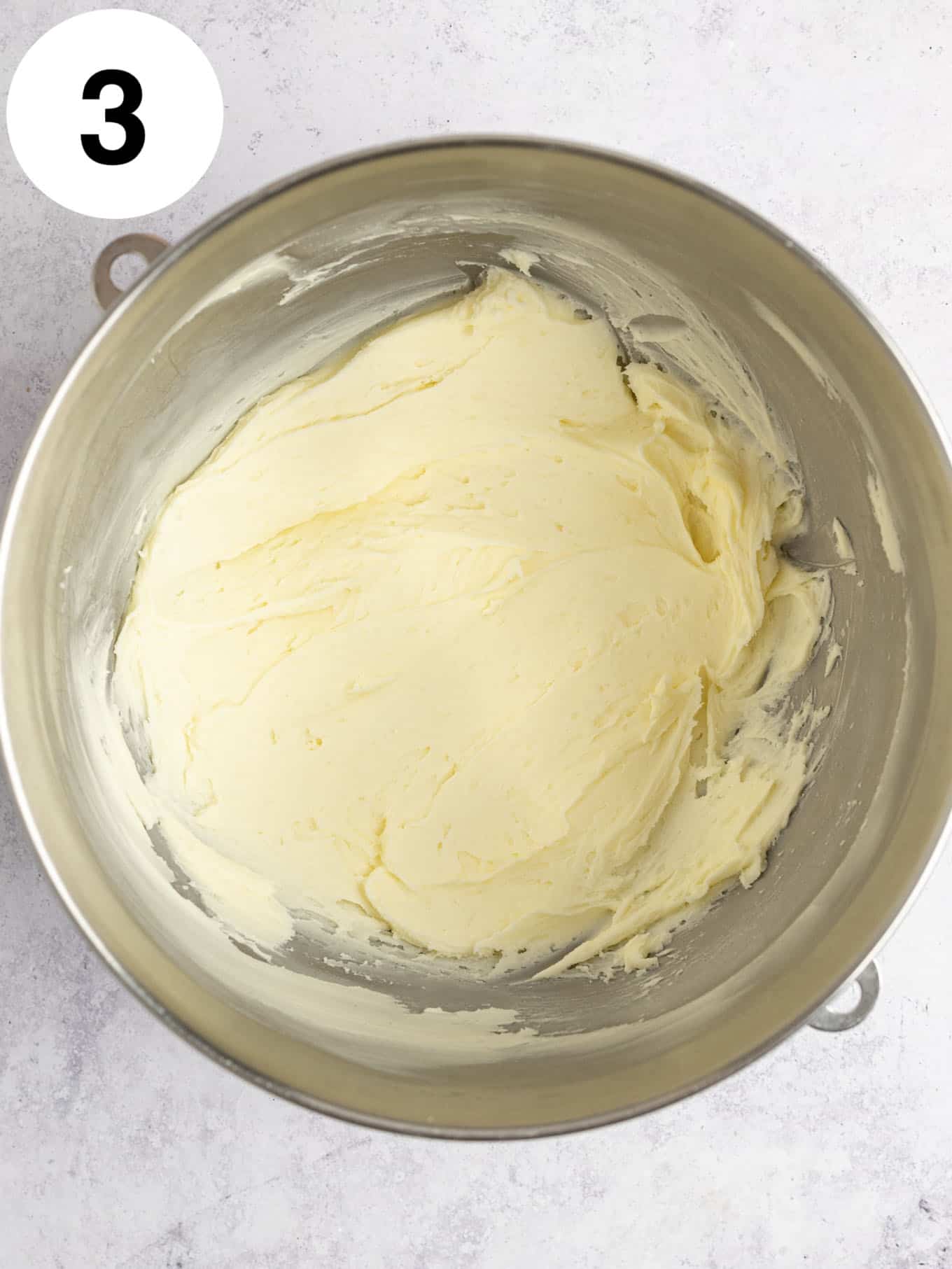 An overhead view of beaten butter and powdered sugar in a mixing bowl. 