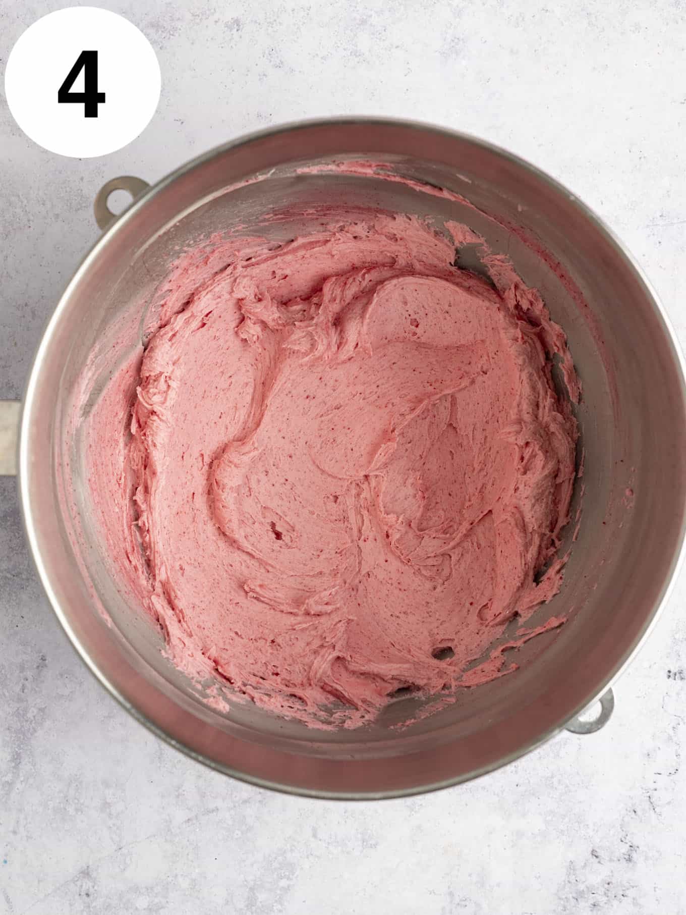 An overhead view of raspberry frosting in a mixing bowl. 