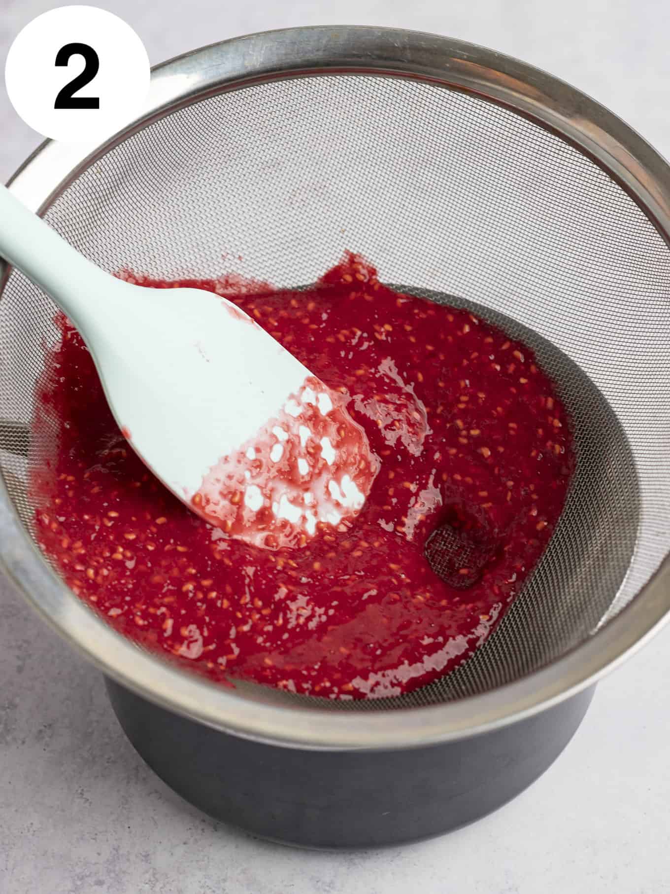 An overhead view of fresh raspberry puree being passed through a mesh sieve. 