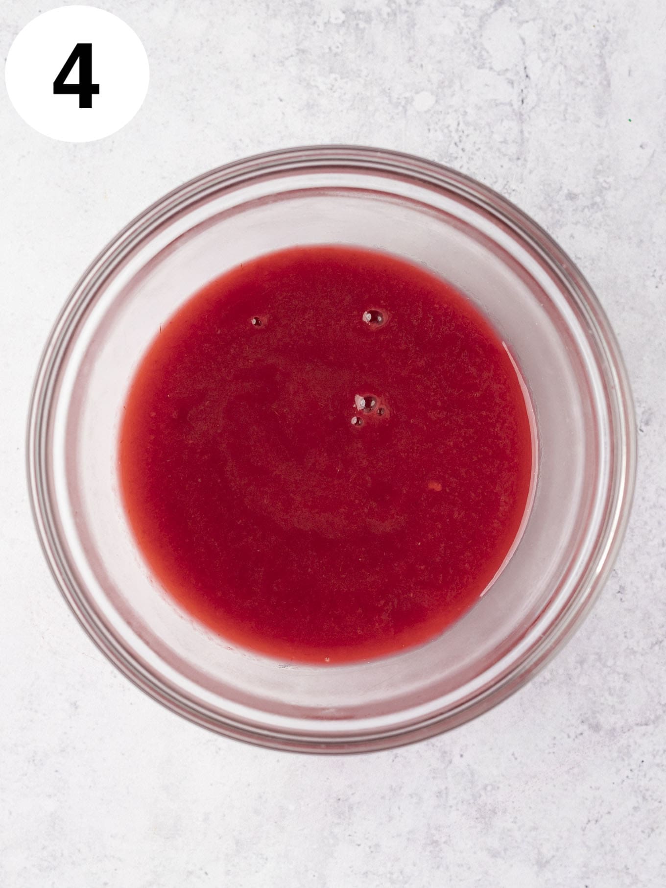 An overhead view of raspberry puree cooling in a glass bowl. 