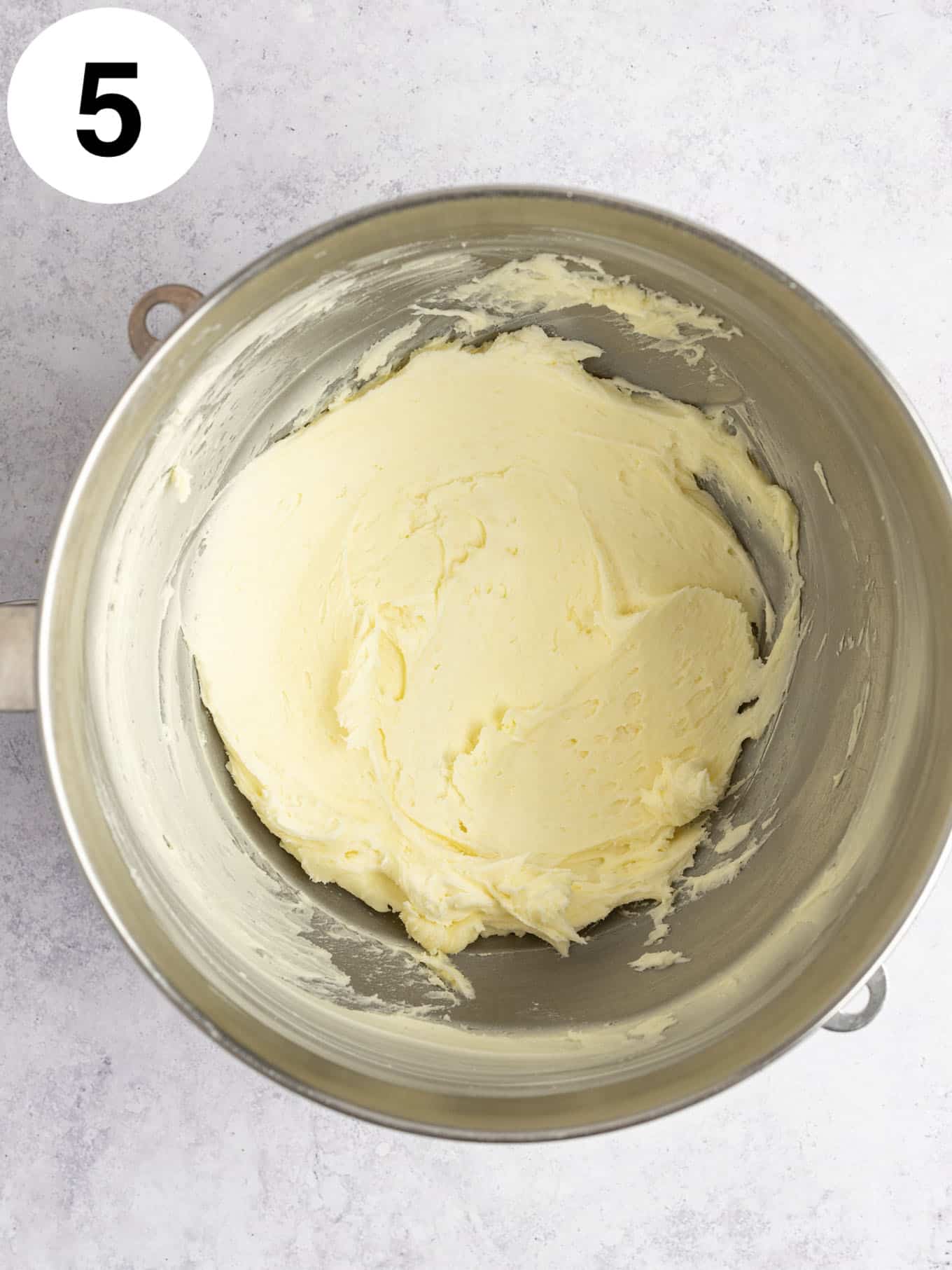 An overhead view of beaten butter and powdered sugar in a mixing bowl. 