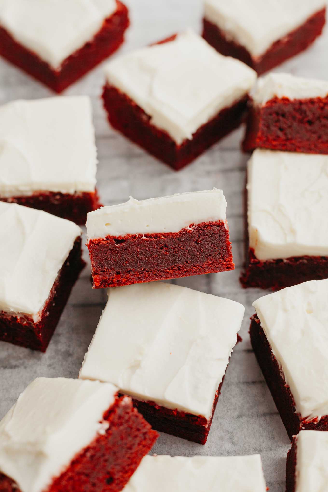 Frosted red velvet brownies sliced and arranged on a wire rack.