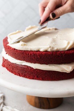 A red velvet layer cake on a cake stand in the process of being frosted.