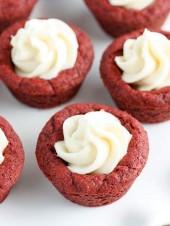 Deep dish red velvet cookie cups with cream cheese frosting on a white plate.