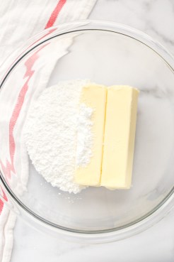 A glass bowl with two sticks of butter and powdered sugar.