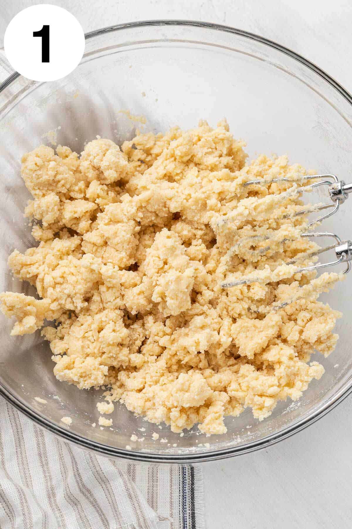 An overhead view of shortbread cookie dough in a glass mixing bowl, with a rubber spatula. 