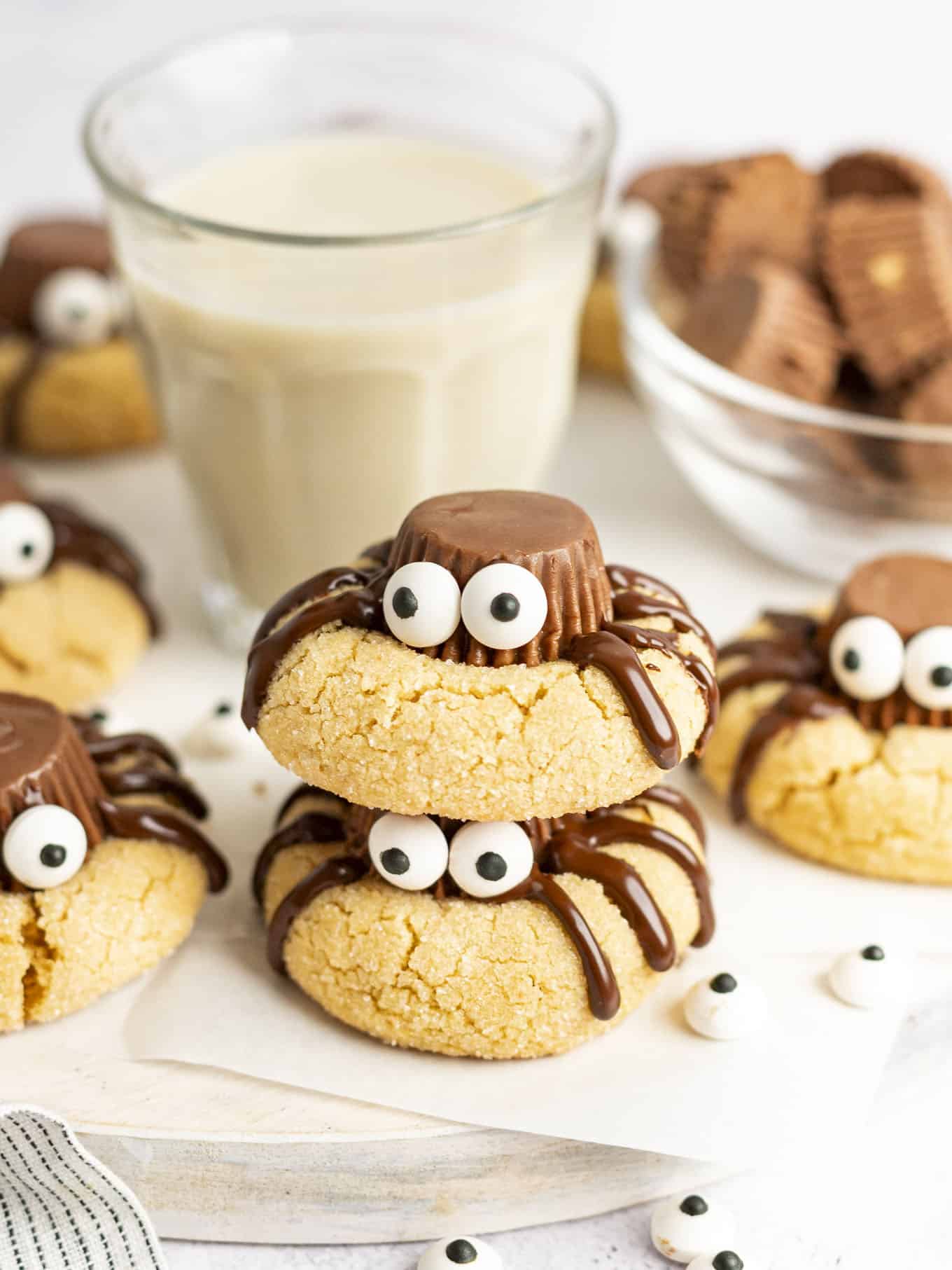 Cute spider cookies stacked around a glass of milk. 