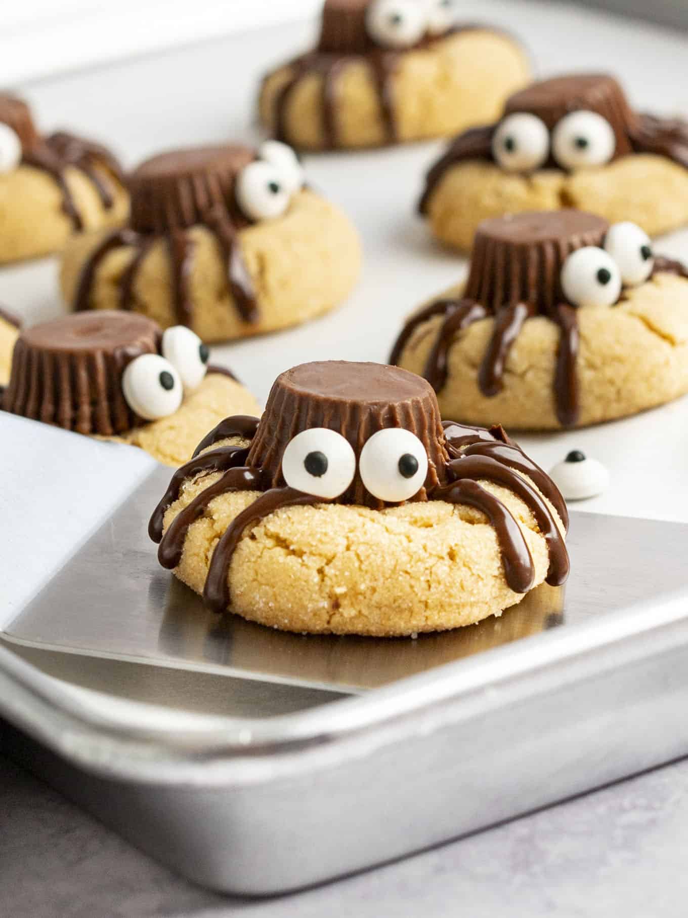 A spider cookie with candy eyes being lifted off a baking sheet. 