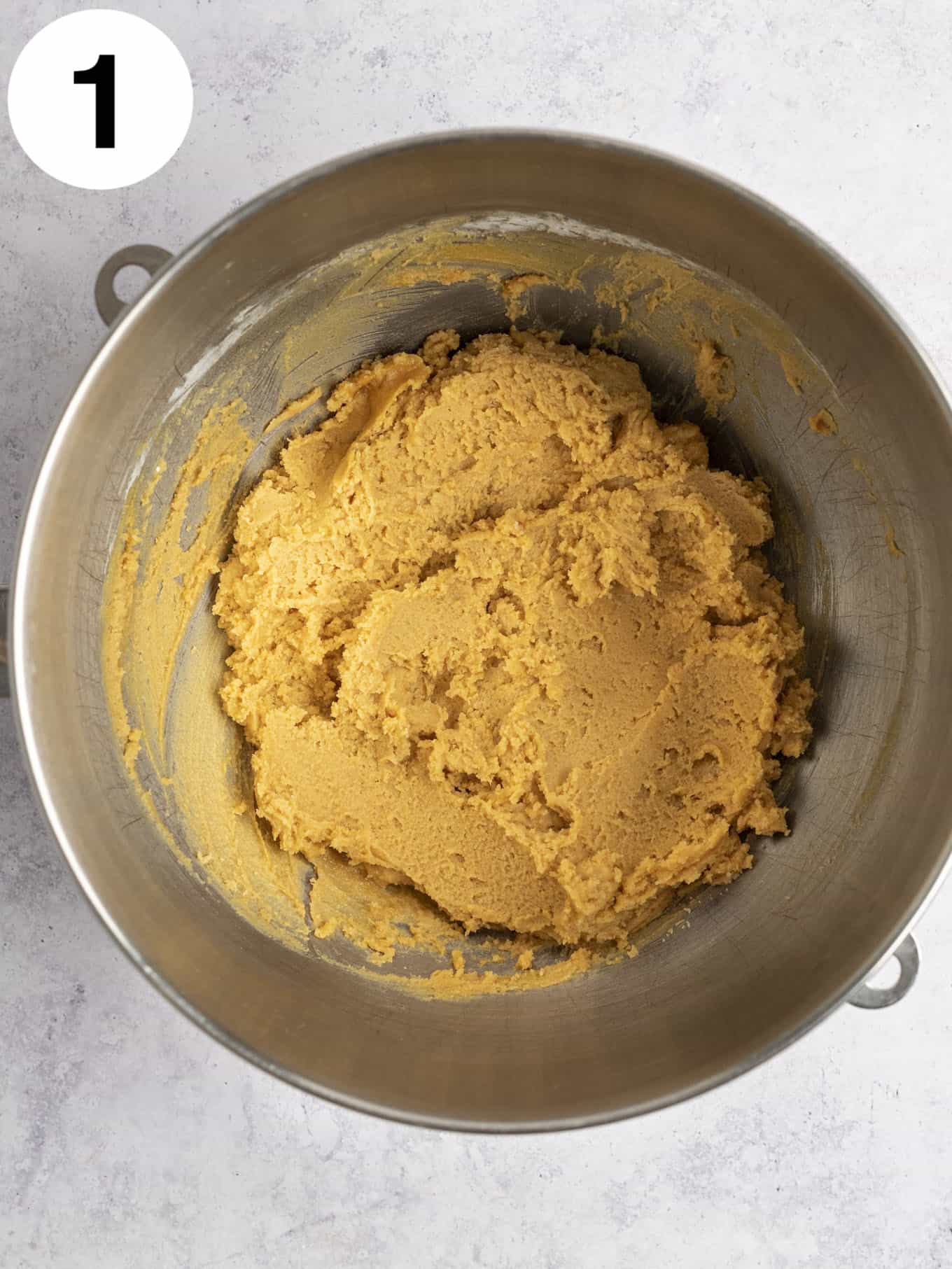 An overhead view of peanut butter cookie dough in a metal mixing bowl. 