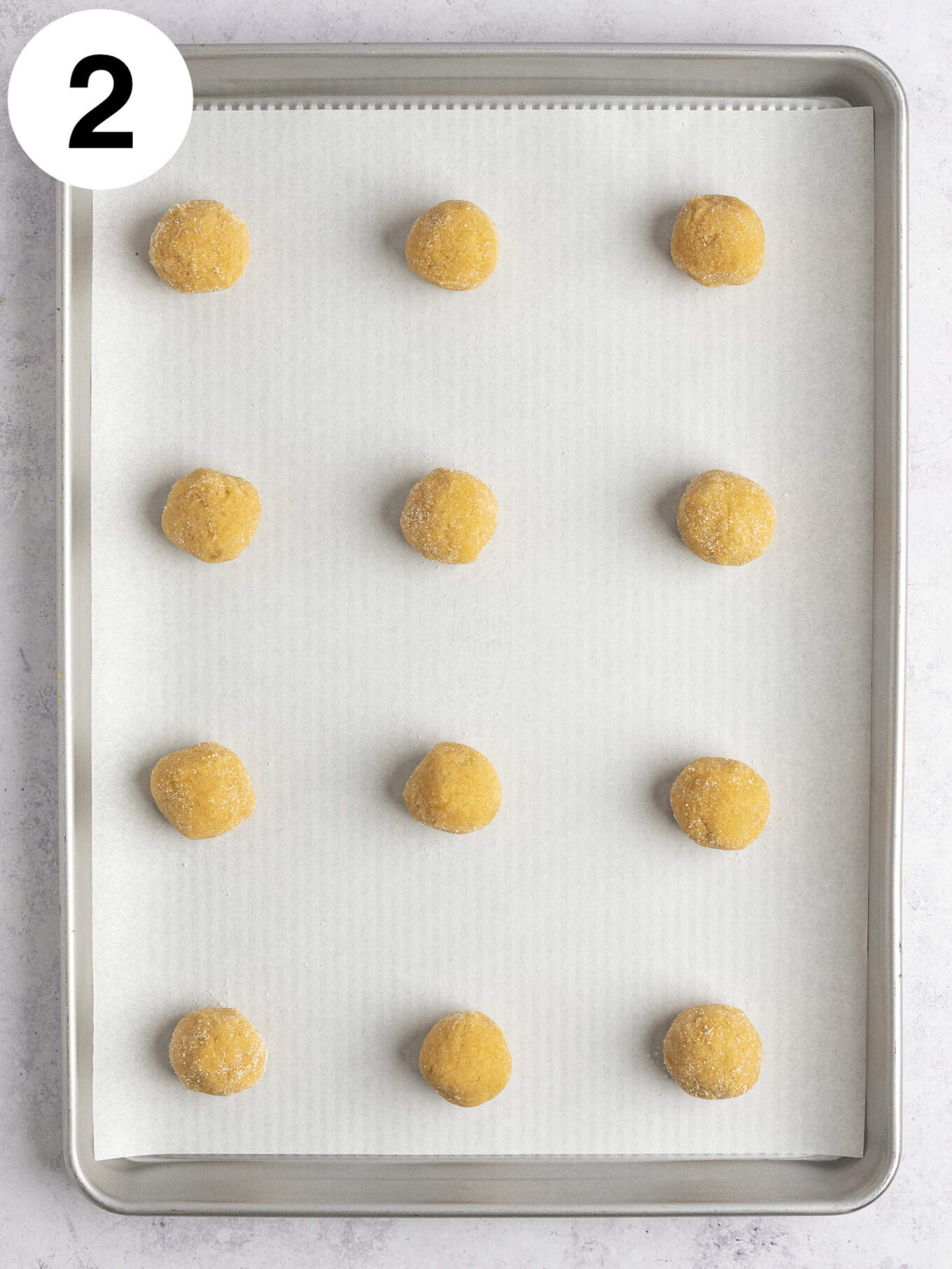 An overhead view of peanut butter cookie dough balls on a parchment paper-lined baking sheet. 