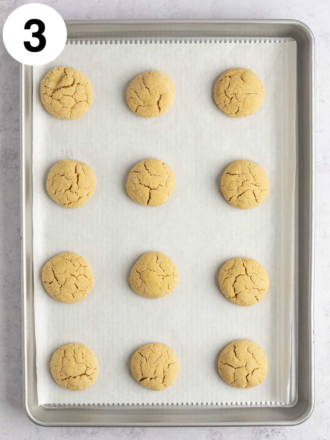 An overhead view of baked peanut butter cookies on a parchment paper-lined baking sheet. 