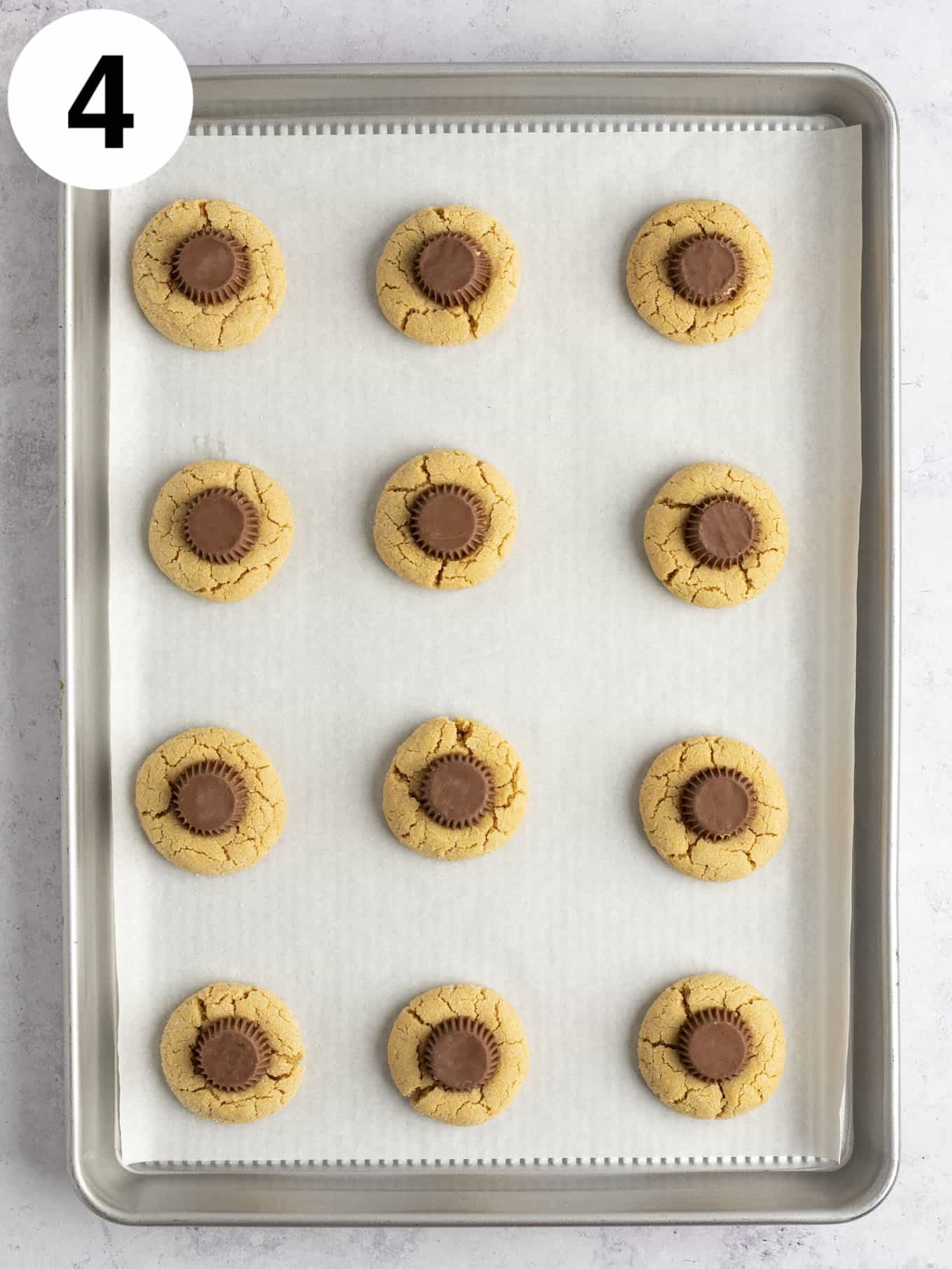 An overhead view of baked peanut butter cup blossom cookies on a parchment paper-lined baking sheet. 