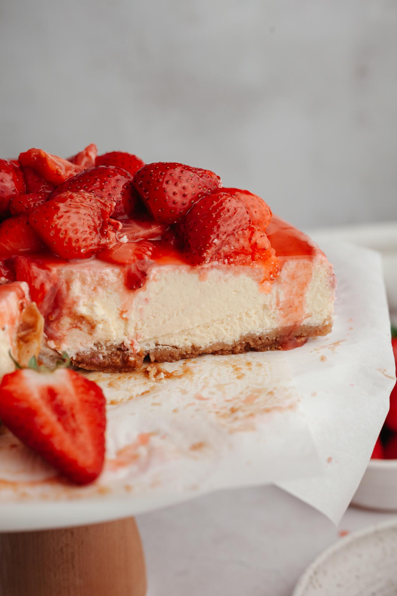 A side view of a sliced strawberry cheesecake on a cake stand. 