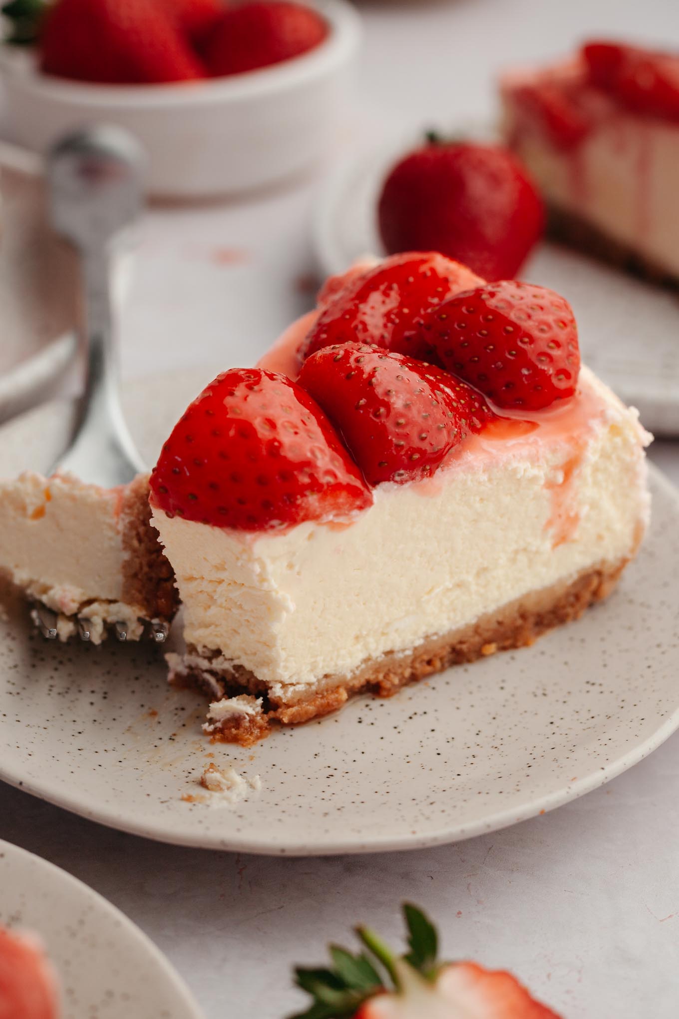 A close-up view of a strawberry cheesecake slice, with a bite speared on a fork. 