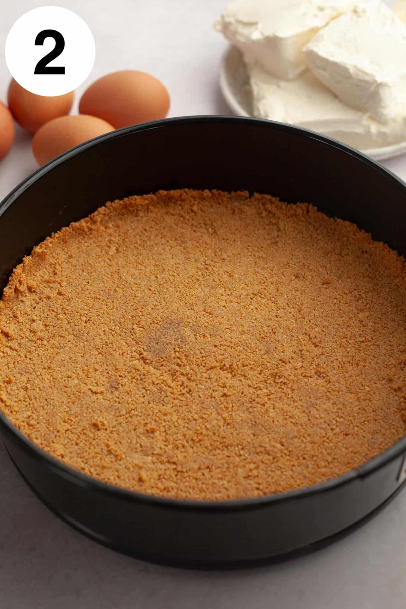 An overhead view of a graham cracker crust in a springform pan. 