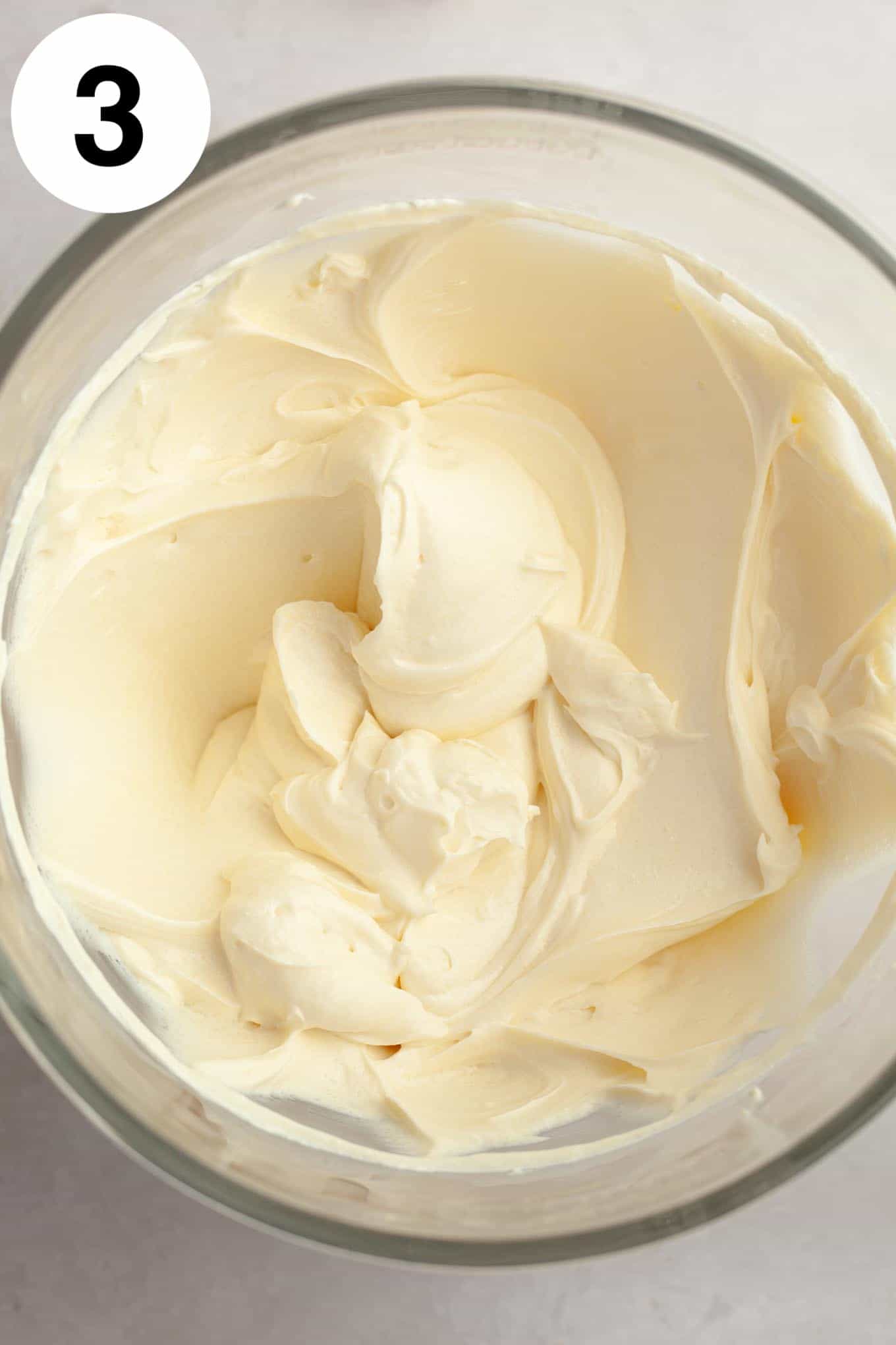 An overhead view of beaten cream cheese and sour cream in a glass mixing bowl. 