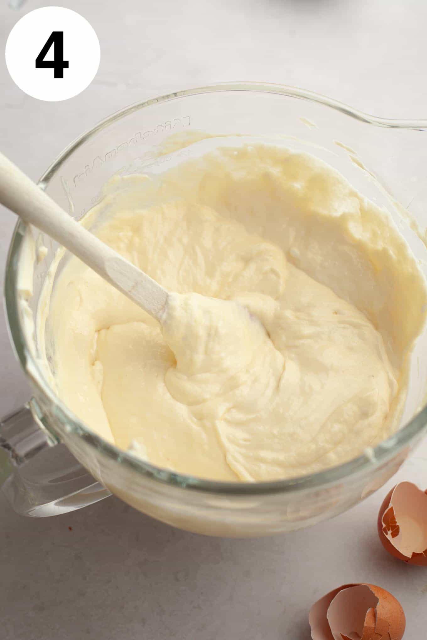 An overhead view of cheesecake filling in a glass mixing bowl. 