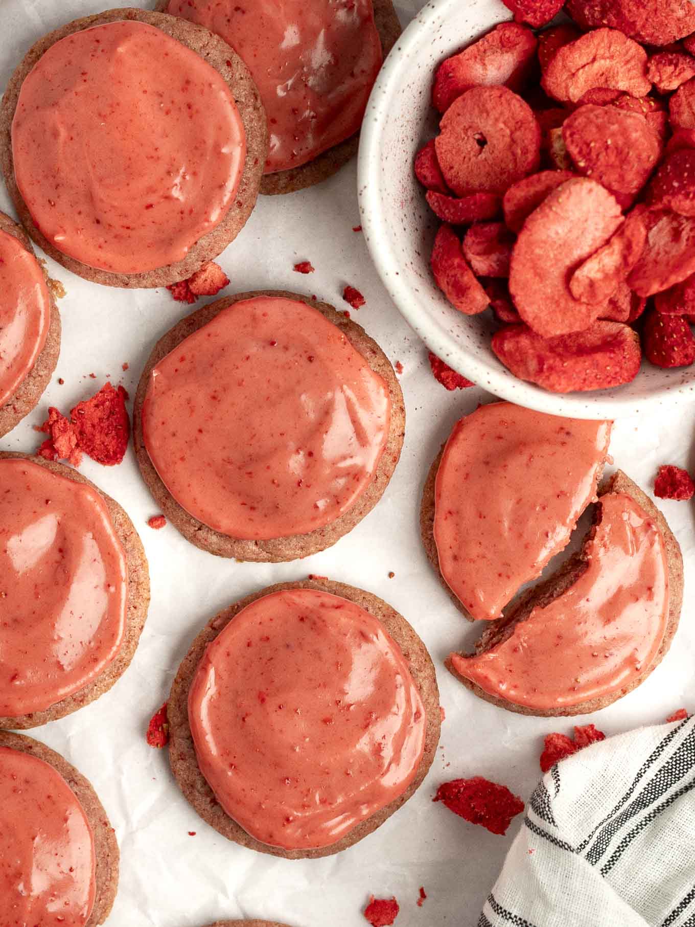 An overhead view of iced strawberry cookies with a dish of freeze-dried strawberries. 