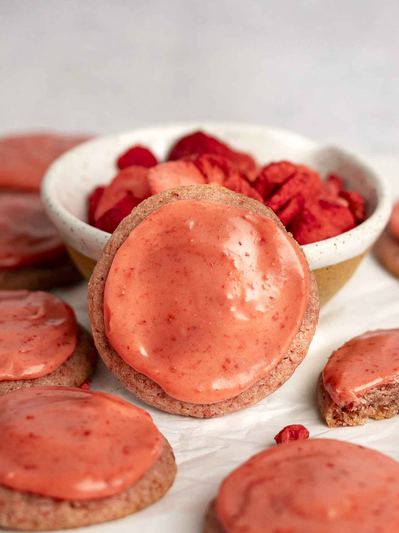 An iced strawberry cookie propped up against a bowl of freeze-dried strawberries.