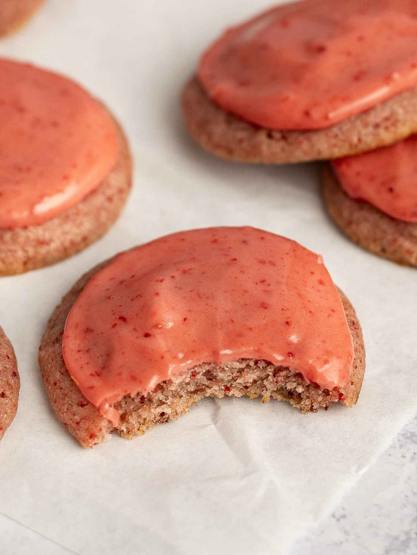 A close-up view of a strawberry cookie with a bite missing. 