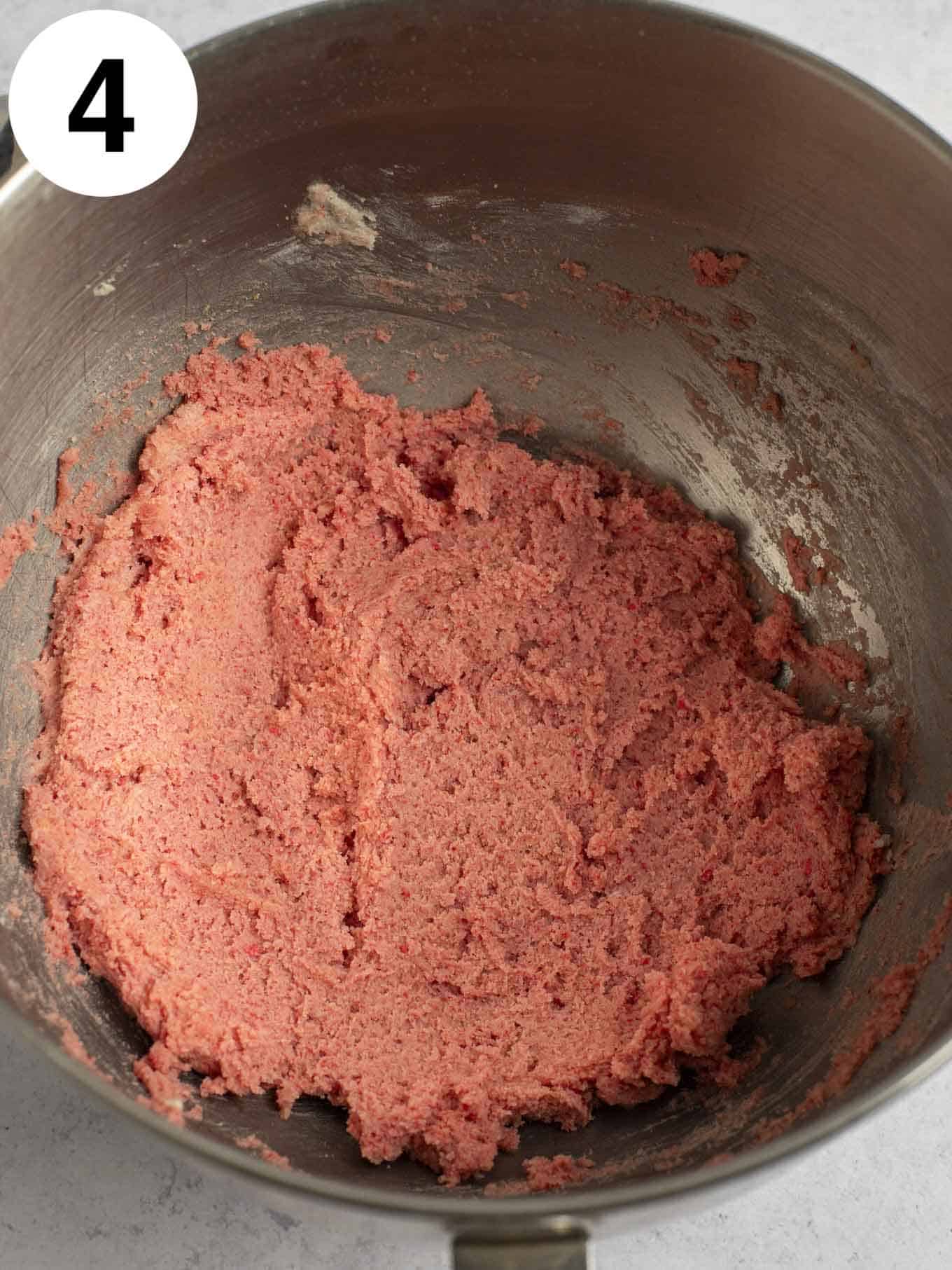 An overhead view of strawberry cookie dough in the bowl of a stand mixer. 