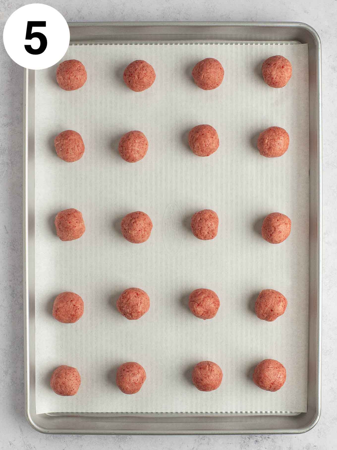 An overhead view of strawberry cookie dough balls on a parchment paper-lined baking sheet. 