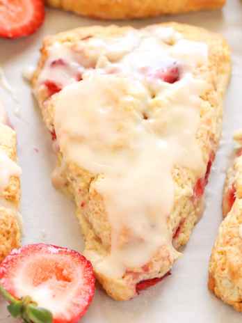 Strawberry scones topped with glaze. Two strawberry halves rest between the scones.
