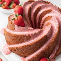 A strawberry pound cake topped with strawberry icing. A few strawberries rest on top of the cake.