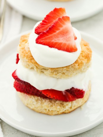 Strawberry shortcake topped with extra whipped cream and strawberries on a white plate.