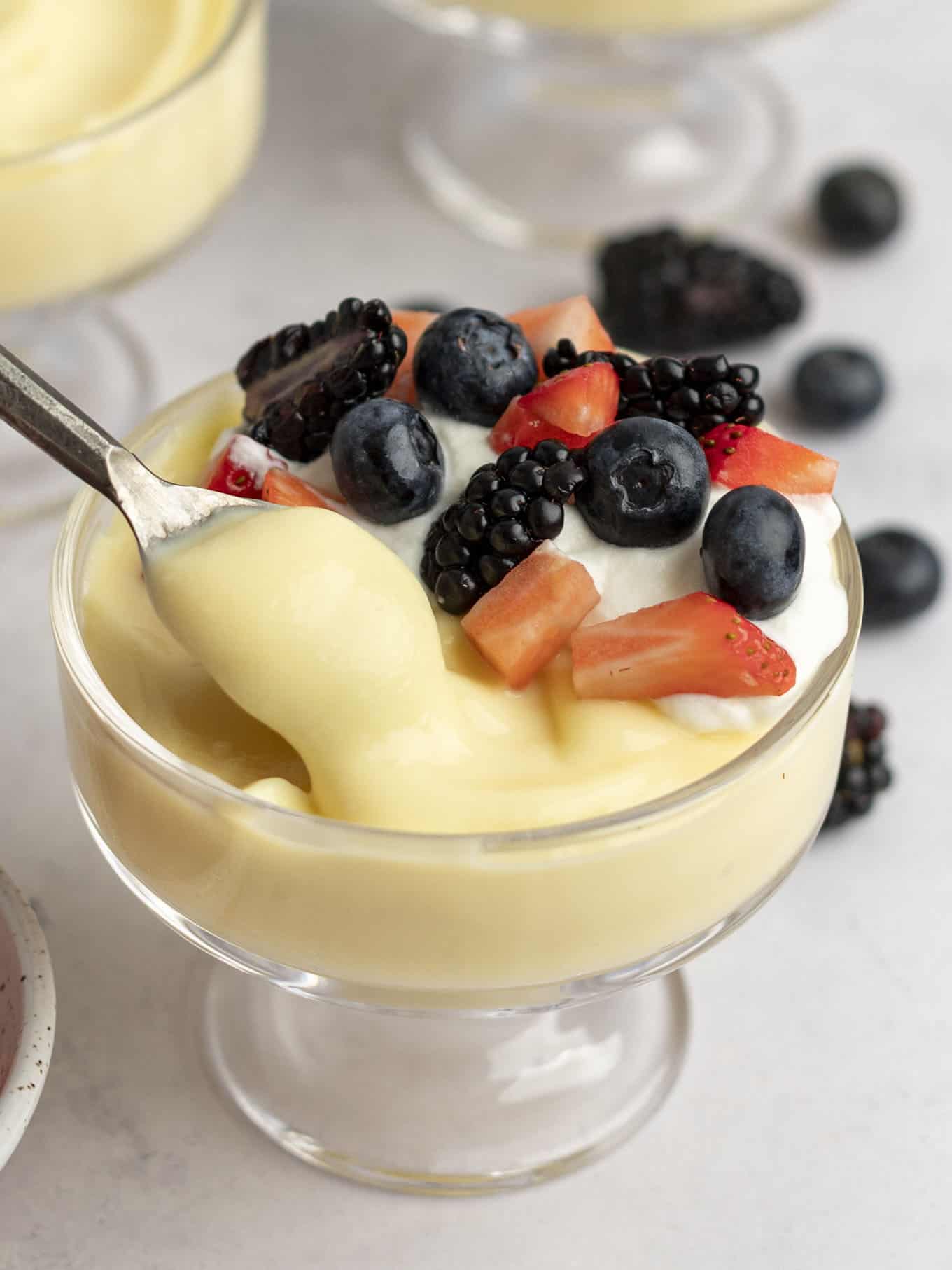 A serving of vanilla pudding being spooned from a glass dish. 
