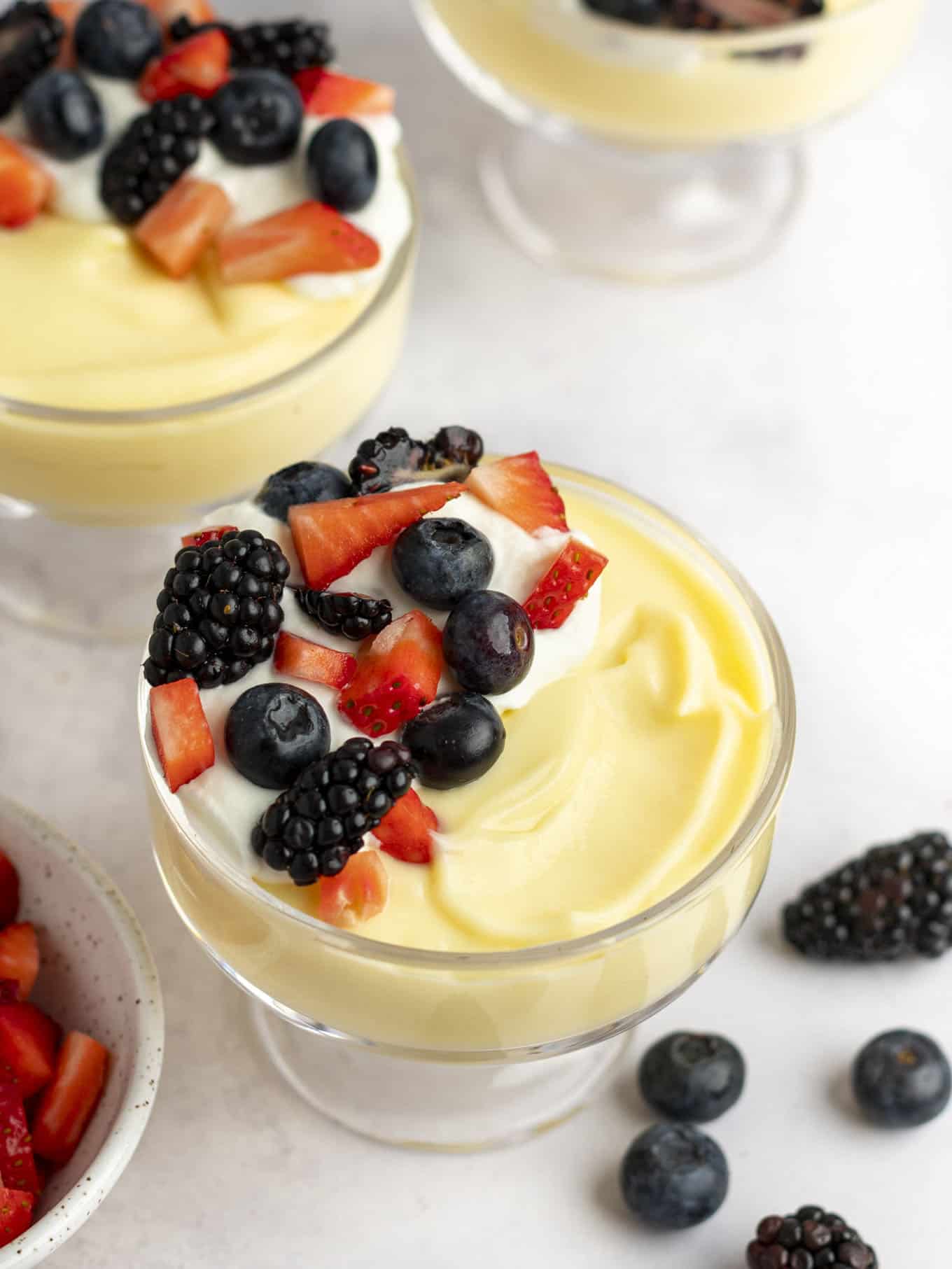 An overhead view of two small dishes full of vanilla pudding, topped with berries and whipped cream.