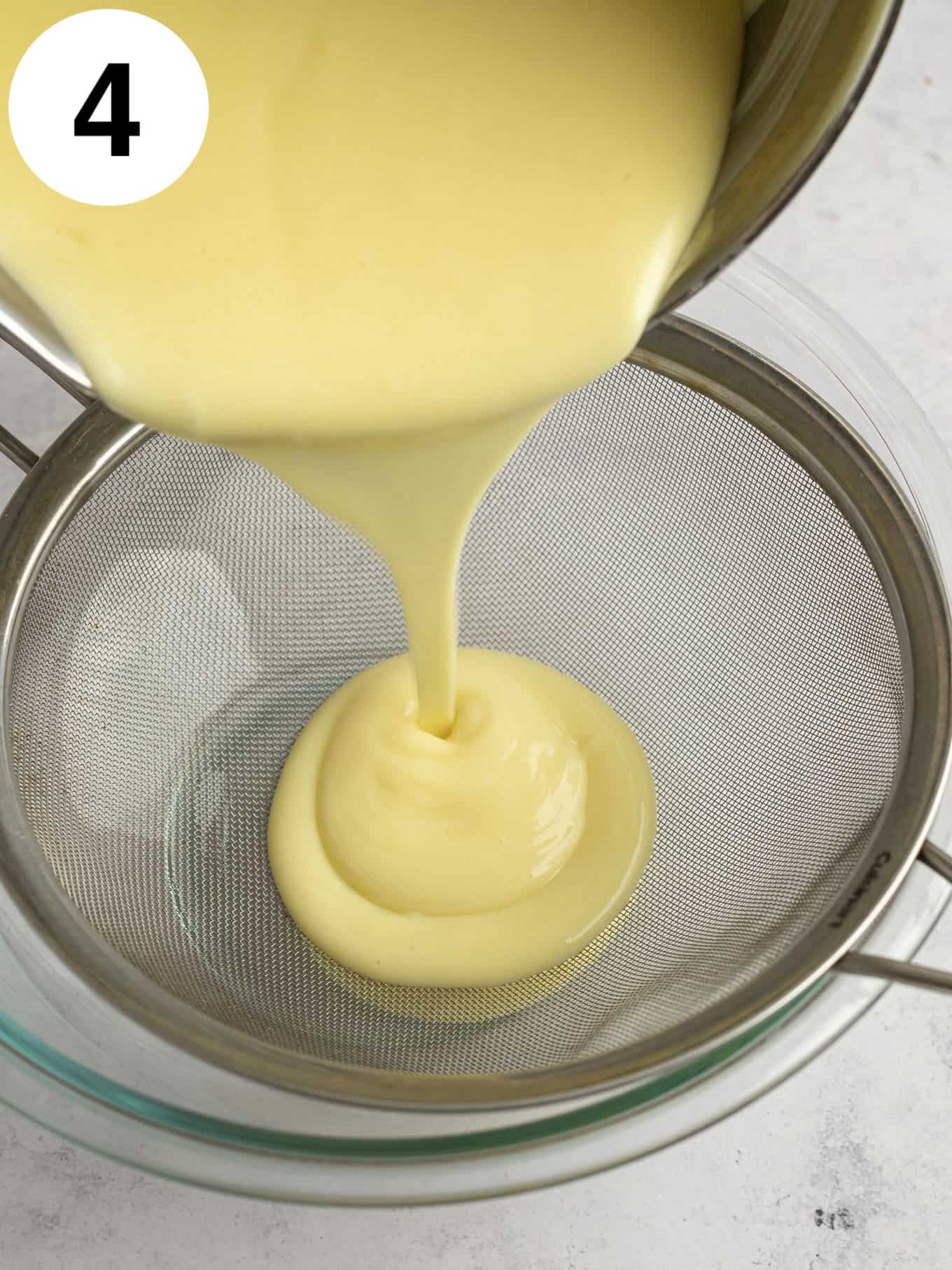 An overhead process shot showing pudding being strained through a fine mesh strainer. 
